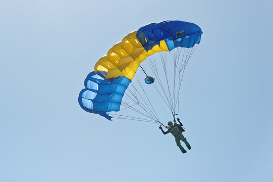 Paraglider flying on colorful parachute in blue clear sky at a bright sunny summer day. Active lifestyle, extreme hobbies