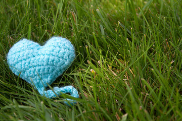 Blue knitted heart lying on green grass background