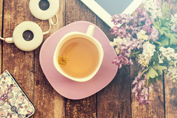 still life with tea cup and the contents of a work space composed. Different objects on wooden table. tablet,phone with headphones and spring flowers
