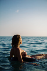 Rear view of unrecognizable young woman with short hair in bikini swimming on air ring with widened arms and looking away at seascape.Copy space
