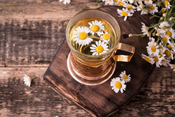 herbal chamomile tea on a wooden table. Chamomile tea in a transparent cup and camomile flowers on wooden table. Herbal tea for baby's stomach. Copy space.