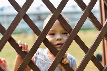 Sad and lonely child looking out through fence. Social problems, family abuse, children stress  negative emotions