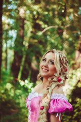 Obraz na płótnie Canvas Beautiful girl with a long braid in pink lace dress smiles in the forest.