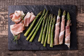 Fresh organic asparagus wrapped in Parma ham on a cutting board