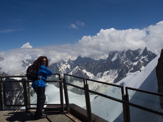 Vistas de una mujer con chaqueta azul mirando el paisaje espectacular de alta monta&ntilde;a con nieve y nubes al fondo de l'Aiguille du Midi en Chamonix Mont Blanc en Francia viajando en verano de 2016