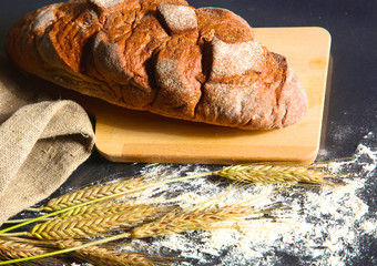 rustic crusty bread and wheat ears on a dark wooden table