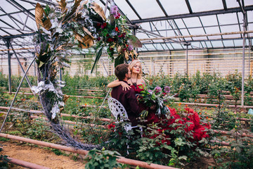 Woman in red cloud dress with man hugging and embracing in greenhouse. 