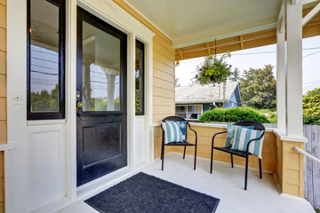 Covered porch with black front door and two wicker chairs.