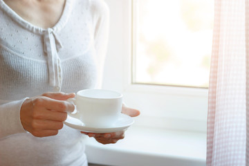 Young woman's hands is holding hot cup of coffee or tea in morning sunlight
