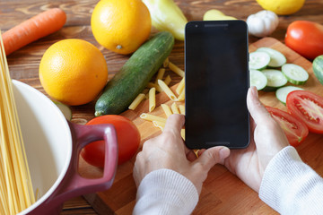 Woman is cooking pasta and looking recipe at smartphone	