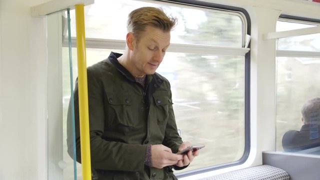 Mature man standing on a train. He is typing on his smart phone.
