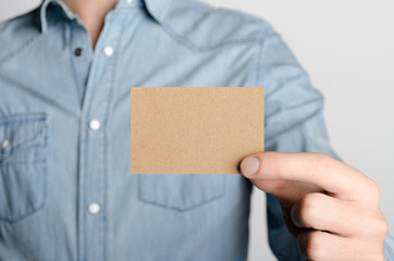 Kraft Business Card Mock-Up (85x55mm) - Man in a denim shirt holding a kraft card on a gray background.