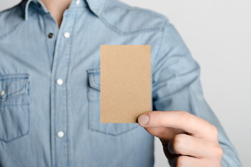 Kraft Business Card Mock-Up (85x55mm) - Man in a denim shirt holding a kraft card on a gray background.