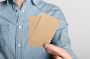 Kraft Business Card Mock-Up (85x55mm) - Man in a denim shirt holding a kraft card on a gray background.