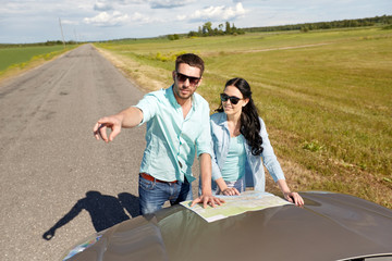 happy man and woman with road map on car hood
