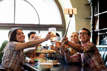 happy friends with selfie stick at bar or pub
