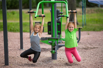 Two funny little girls is engaged in sports equipment outdoor.