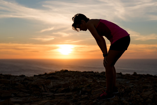 Side view of a exhausted and tired woman silhouette at sunset after running workout taking a rest