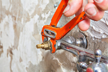 Close-up of hands plumber turning tap valve with red pliers.
