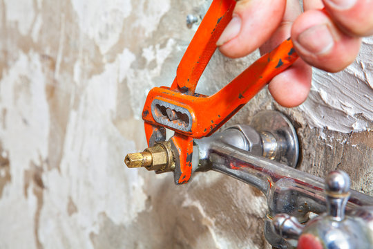 Close-up of hands plumber turning tap valve with red pliers.
