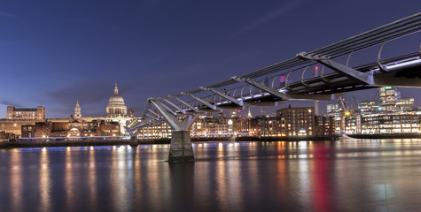 Fototapeta na wymiar St Paul's Cathedral and the Millennium Bridge over the Thames, at night, with the lights shining on the opposite shore