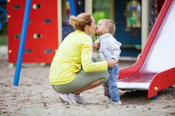 Fototapeta na wymiar Mother kissing son after catching him at bottom of playground slide