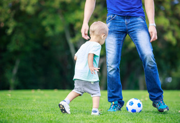 Young man and toddler son playing football in park