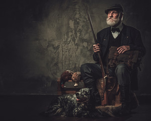 Senior hunter with a english setter and shotgun in a traditional shooting clothing, sitting on a...