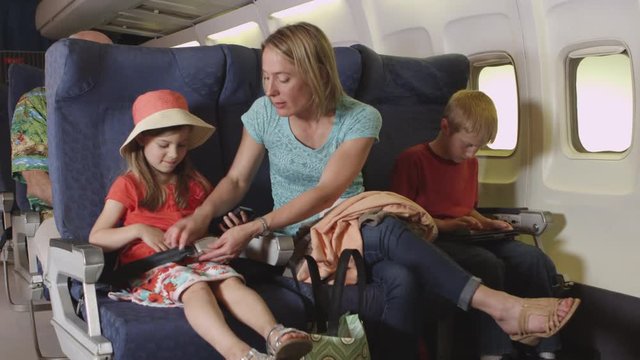 Mother buckling her children into seats on plane