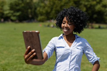 Black woman in a park using tablet computer selfie
