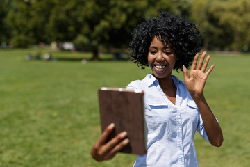 Black woman in a park using tablet computer selfie
