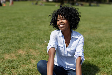 Black woman in a park sitting on lawn happy
