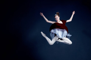 Fototapeta na wymiar Young ballerina in a beautiful dress is dancing in a dark photostudio