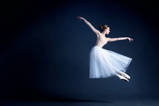 Fototapeta Young ballerina in a beautiful dress is dancing in a dark photostudio