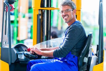 Verkäufer im Baumarkt fährt Gabelstapler im Lager für Handwerker-Bedarf