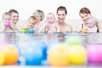 Mamas und Neugeborene spielen beim Säuglingsschwimmen mit Bällen