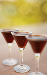 Three glasses of liquor on wooden table outdoors closeup