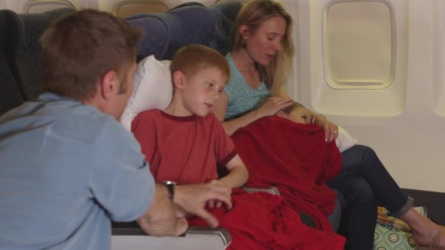 Family tucking in children to sleep on plane