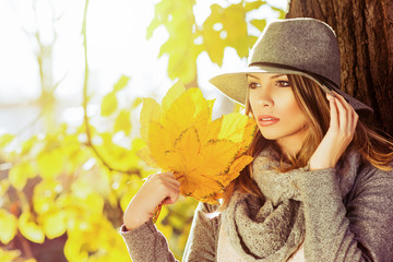 Gorgeous young woman wearing gray autumn outfit outdoors in park on sunny fall day