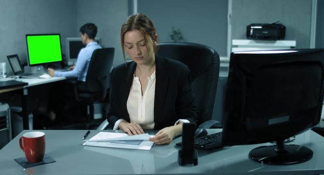 4K: Eine junge Managerin analysiert einige Finanzberichte in einem B&uuml;ro. Eine andere Kollegin arbeitet im Hintergrundgrund an einem chroma gr&uuml;nem Monitor.
