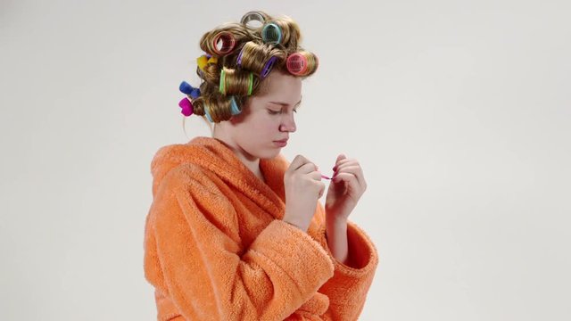 Teenage girl wearing bathrobe in hair curlers applying nail polish on fingernail