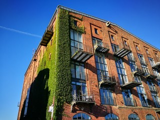Saniertes altes Speichergebäude aus Backstein mit begrünter Fassade vor blauem Himmel im...