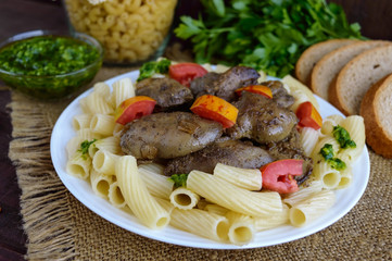 Pasta and fried goose liver (chicken, duck) with pesto and tomato on a wooden background.