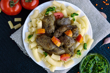 Pasta and fried goose liver (chicken, duck) with pesto and tomato on a black background.