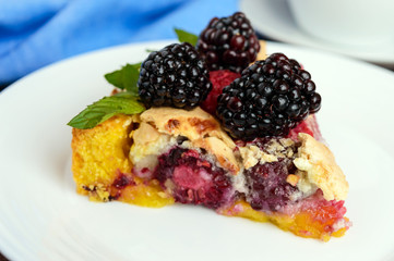 A piece of the pie (Tart) with fresh blackberries and raspberries, air meringue, mint decoration on a white plate