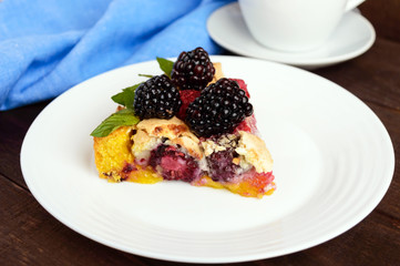 A piece of the pie (Tart) with fresh blackberries and raspberries, air meringue, mint decoration on a white plate