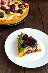 A piece of the pie (Tart) with fresh blackberries and raspberries, air meringue, mint decoration on a white plate