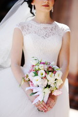 beautiful bride with a wedding bouquet in hands on a background of a wall