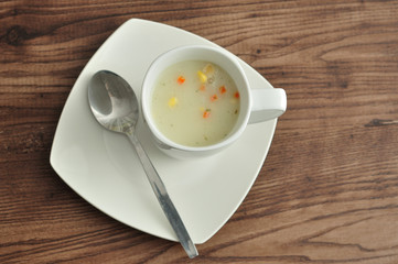 A mug of vegetable soup displayed with a spoon and plate 