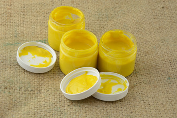 Opened jars of yellow turmeric tahini sauce or paint on burlap